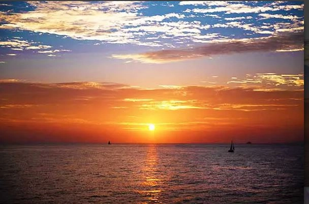 Golden sunset over ocean with sailboats